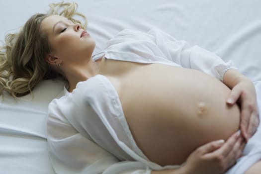 Young pregnant girl with blonde locks lying in bed cropped high angle shot