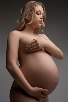 Young pregnant woman with blonde locks nude cropped shot on gray background