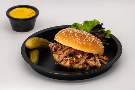 A delicious and mouthwatering pulled pork sandwich that is expertly served with crunchy pickles and a tangy mustard dip