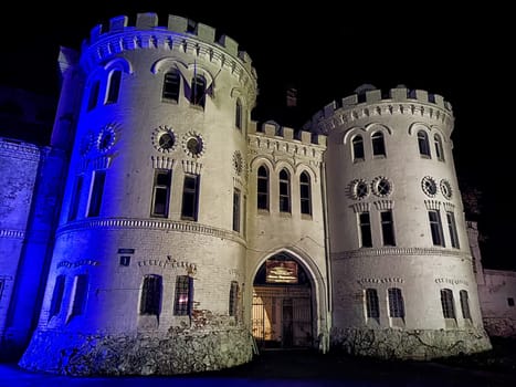 A view of Sheremetyevo Castle, illuminated at night in Russia. The castle's stone walls and towers are lit in soft blue light
