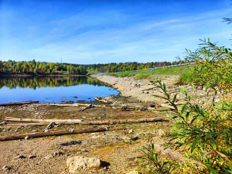 A serene lake stretches out beneath a blue sky with scattered clouds, framed by a grassy hillside.