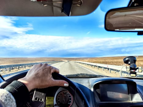 Car salon, windshield, hand of woman on steering wheel and landscape. View from seat of driver on nature landscape. Single trip of female traveler