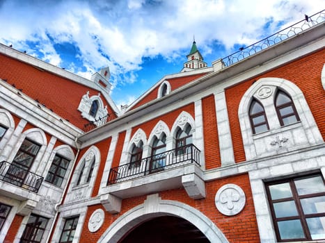 A beautifully designed red brick building under a partially cloudy sky showcases intricate architectural details. The facade of house with turrets