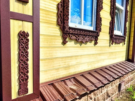 Beautifully crafted wooden details frame the windows and border the base of a sunny yellow house, highlighting traditional design.