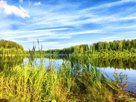 The river reflects the vivid blue sky filled with wispy clouds, framed by verdant trees on both sides, creating a tranquil vista.