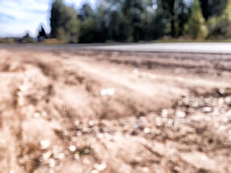 A dusty road stretches into the distance, bordered by lush greenery and a blue sky, depicting a peaceful rural landscape.