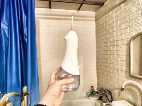 A hand grips a dental irrigator designed for oral hygiene, displayed in a bright bathroom environment with relevant accessories.