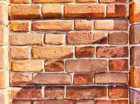 Rustic red bricks form a textured wall, displaying color variations and natural patterns under bright sunlight.