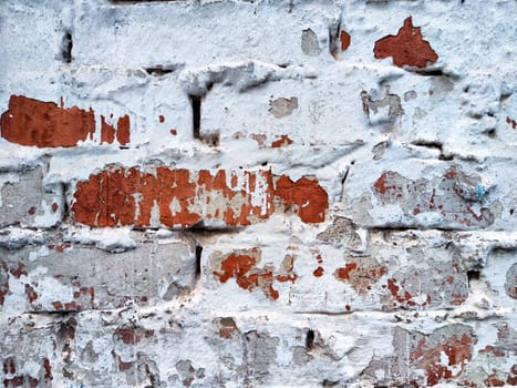 A brick wall shows signs of peeling paint with red and white hues in an urban environment.