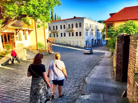 Sighnaghi, Georgia - June 06, 2024: Two women stroll leisurely down a charming cobblestone street lined with colorful buildings on a bright, sunny afternoon.