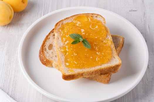 Toasts with tasty apricot jam on a white wooden table.