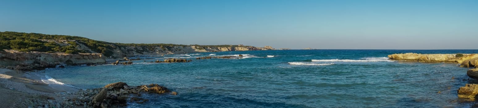 Waves gently caress the rocky shoreline, reflecting hues of blue and gold as the sun sets on the horizon.