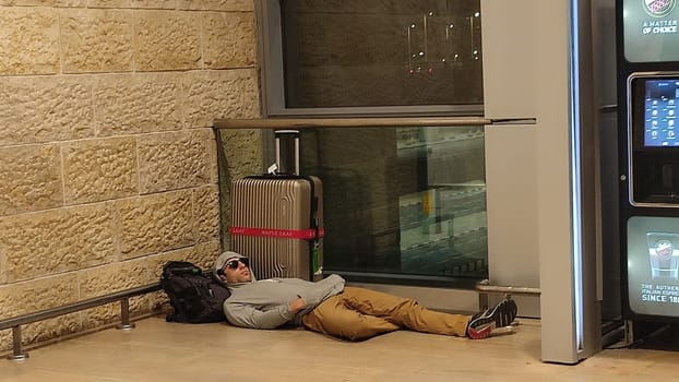 15 October 2024 Tel-Aviv Israel Ben Gurion airport Terminal 3, travel lounge, Male tourist sleeping on the floor near a suitcase, quality photo