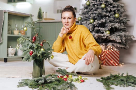 Woman in yellow sweater decorating small Christmas tree with toys in cozy home atmosphere. merry christmas
