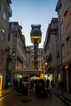 Portugal, Lisbon, 16 january 2023 Elevator de Santa Justa in Baixa in the City of Lisbon in Portugal. Night city lights glow people sit in street restaurants drinking wine