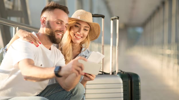 Vacation Begins. Happy couple taking selfie with tickets, waiting for a flight in the airport building