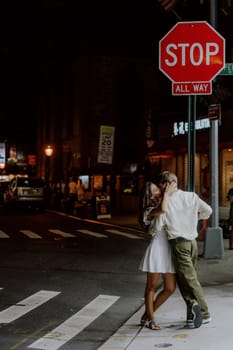 A lovely couple shares a romantic moment under the bright city lights while standing at a stop sign crossing