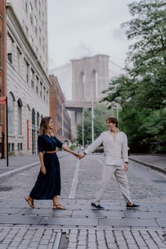 A couple joyfully walks together in New York City, with the stunning Brooklyn Bridge in the background
