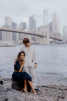 A fashionable couple joyfully shares a moment by the picturesque water, with a breathtaking city skyline behind them. Brooklyn bride and Manhattan in New York.