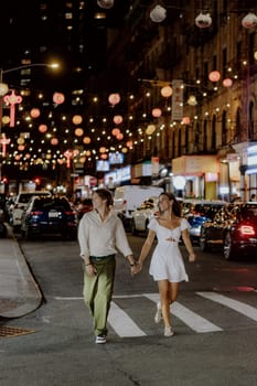 A charming couple leisurely strolls through a bustling city street, which is beautifully adorned with vibrant lanterns
