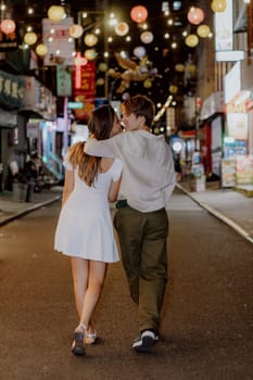 A couple enjoys a lovely stroll, hand in hand, beneath the colorful lanterns adorning the vibrant city streets