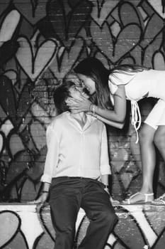 A couple kisses in front of a vibrant heart mural, symbolizing their love in a lively urban setting