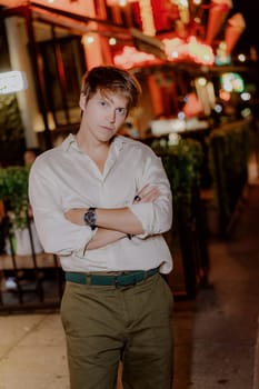 A fashionable and stylish young man confidently poses in an urban setting during the vibrant night hours