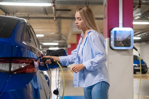 Woman plugs in an electric car for charging in an underground parking facility during daylight.