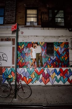 A couple kisses in front of a vibrant heart mural, symbolizing their love in a lively urban setting