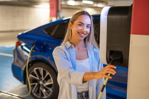 Woman connects her electric car to a charging station in a parking garage