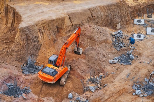 modern orange excavator digs the ground under the foundation pit at a construction site