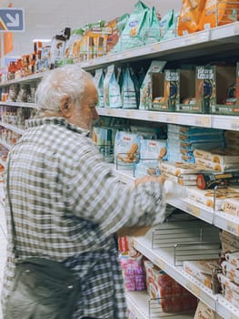 Cremona, Lombardy, Italy October 15th 2024 Elderly man shopping for cookies in a supermarket, carefully checking the packaging information before making a purchase