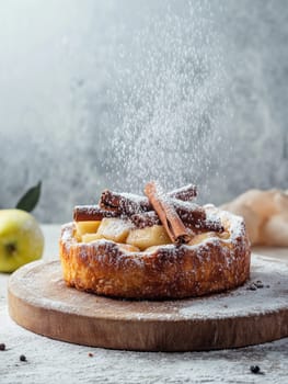 Delicious warm apple pie with cinnamon sticks and a dusting of icing sugar on wooden board.