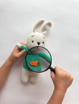 Child examining crochet bunny with magnifying glass.