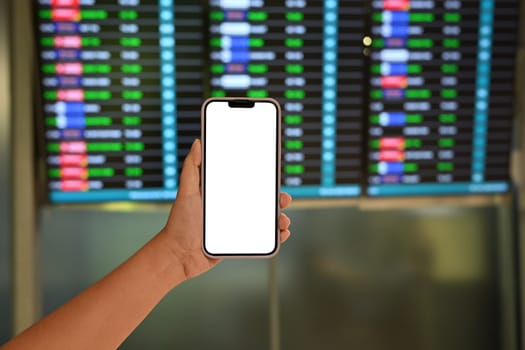 Traveler holding a smartphone with blank screen against airport flight board.