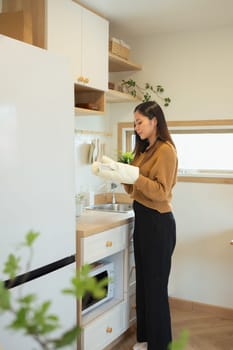 Beautiful woman holding a freshly baked dish with oven mitts, ready to serve.