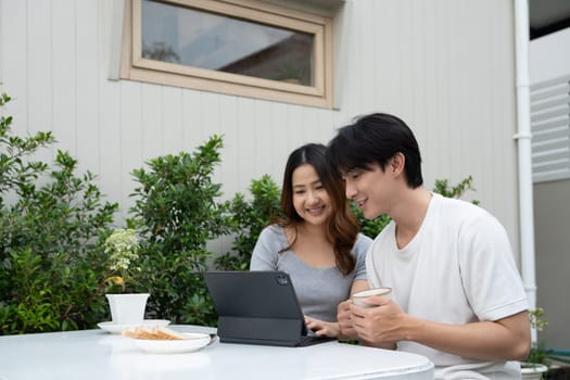 Happy young Asian couple using digital tablet and spending time together in backyard.