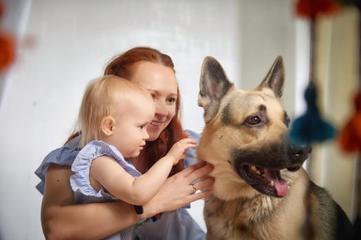 A woman holds a toddler in her arms as they both look at German Shepherd dog