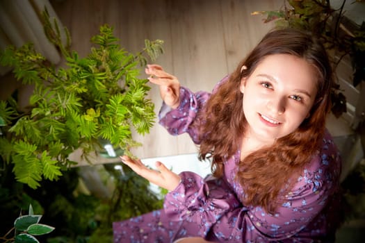 The young woman smiles while reaching out to touch the lush green leaves in her serene indoor garden setting.
