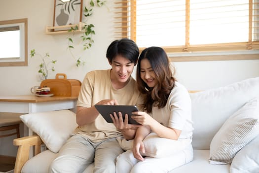 Happy young couple in casual wears watching online content on digital tablet at home.