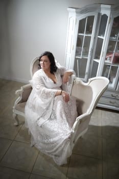 A woman in a flowing white dress relaxes gracefully on an antique sofa, capturing a romantic ambiance in a softly lit room.