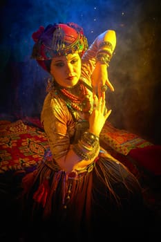 A woman in a colorful headscarf and jewelry poses in front of wall of colorful tassels