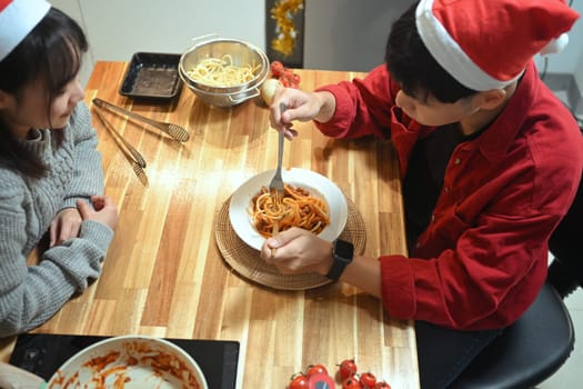 Above view of young couple in Santa hats enjoying a warm holiday dinner in the kitchen.