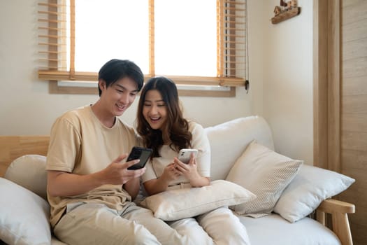 Relaxed asian couple watching online content on a smart phone in the living room.