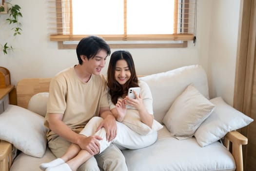 Young cheerful love couple sharing content on a smartphone together at home.