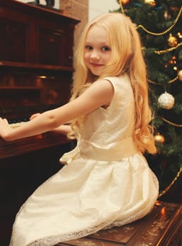 Portrait of little girl child playing on piano at home near christmas tree