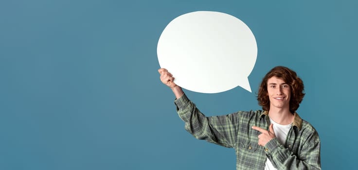 Communication concept. Cheerful curly guy pointing at speech bubble on color background