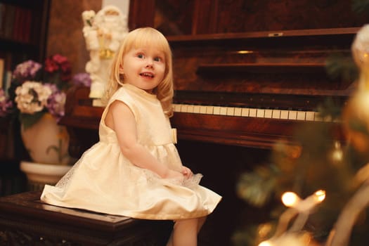 Portrait of happy smiling little girl child playing on piano at home near christmas tree