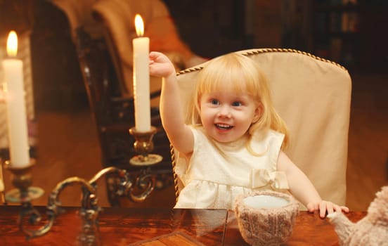 Christmas night, happy joyful little child makes a wish sitting at the table with sweets and burning candles at home, holiday background