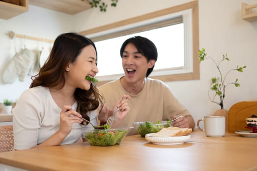 Happy asian couple sharing a fresh and healthy salad meal in a cozy kitchen.